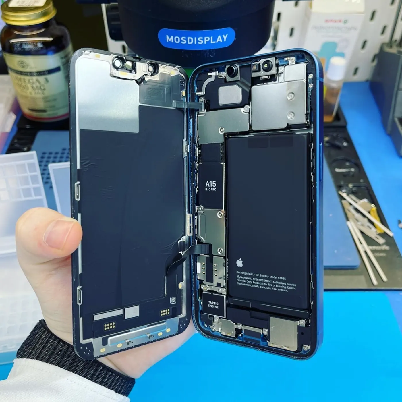 iPhone с откинутым экраном в руке мастера Мосдисплей: виден аккумулятор