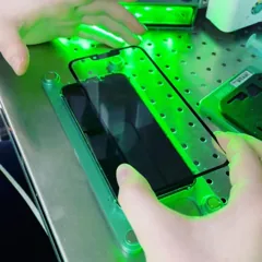 Мастер совмещает новое стекло с экраном iPhone под зелёной подсветкой
